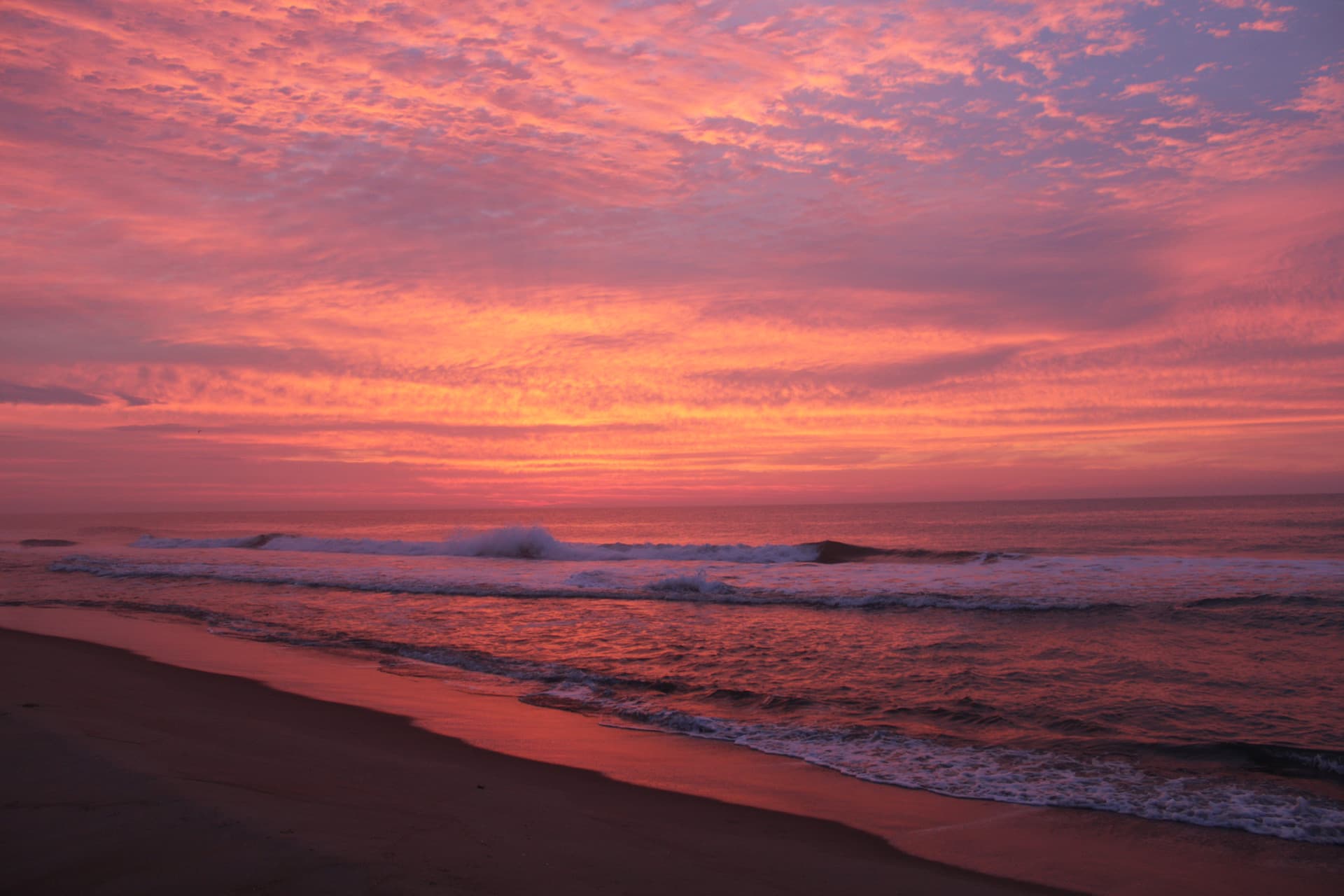 A pink sunrise shining on the beach in OC, MD.